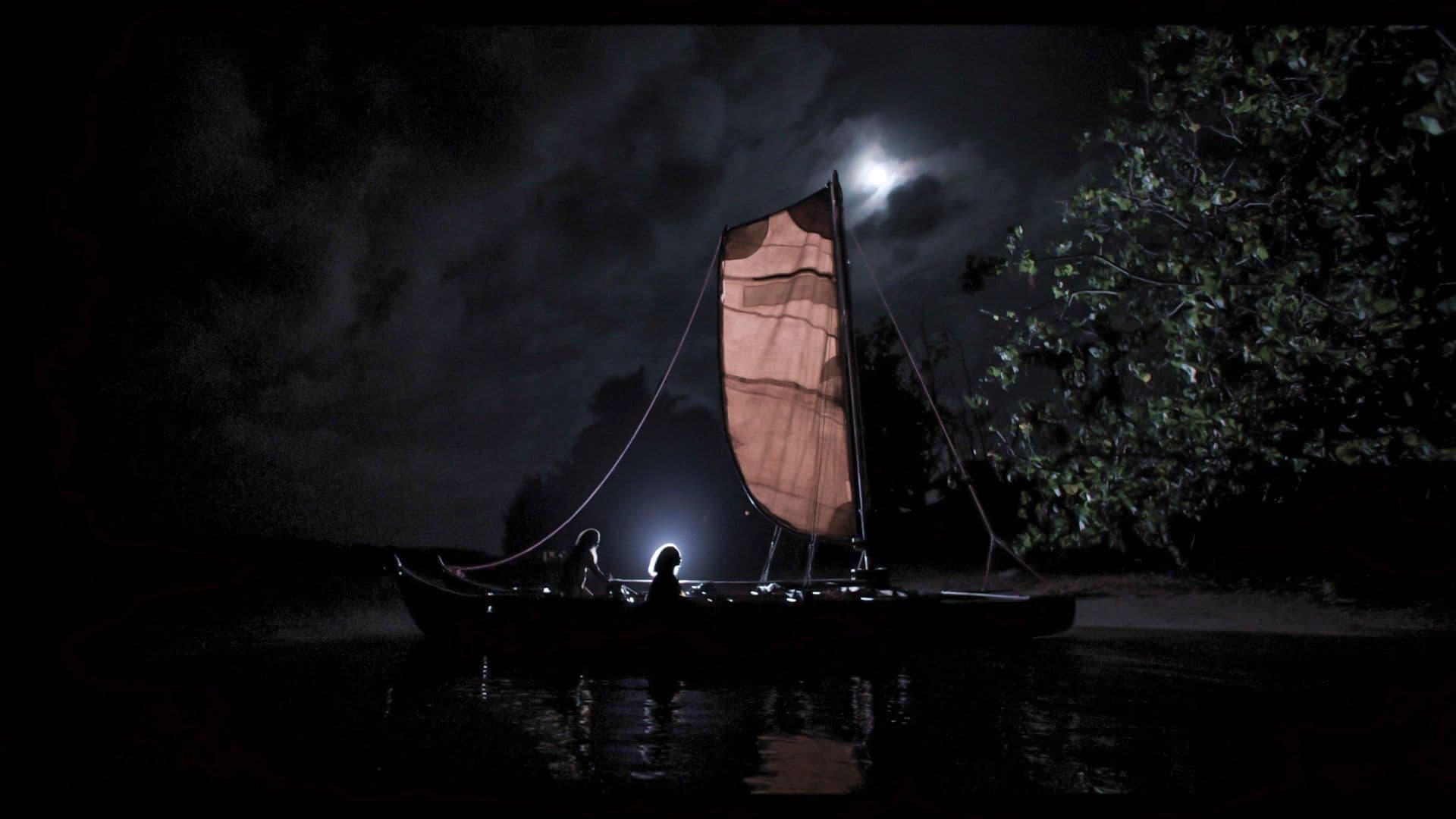A traditional outrigger sailing canoe glows warmly at night on a moonlit lagoon, its triangular sail lit from within beneath a cloudy sky.